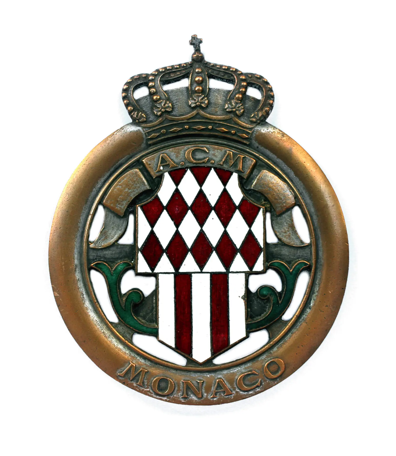 A not often seen early grille badge of the Automobile Club de Monaco (ACM). Like most Monegasque pieces, it is very fine, with the shield decorated with red diamonds, floral details on both sides, in green enamel, and topped with the Princely Crown. Diameter 9cm. Condition good+, with some traces of the silver plated finish, and the cross at top slightly bent.